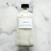 Facial cleanser in a clear glass bottle with green powder and black lid, ANITAKO label visible