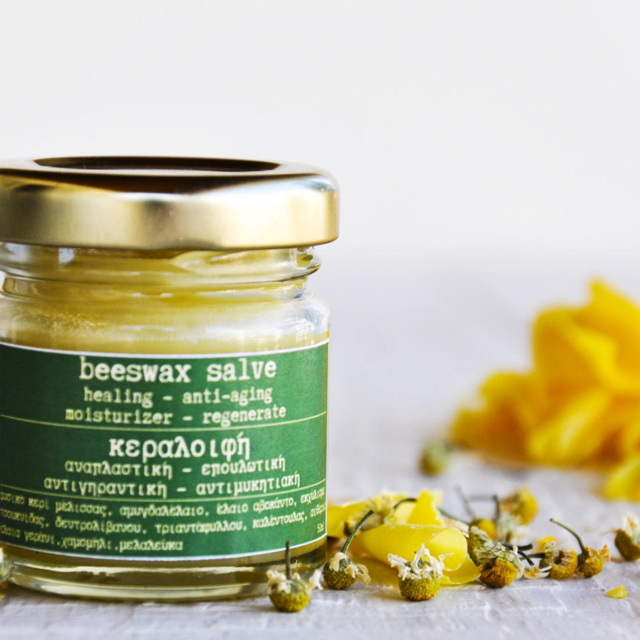 Beeswax salve jar with gold lid, green label, and yellow salve inside, with flowers