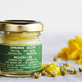 Beeswax salve jar with gold lid, green label, and yellow salve inside, with flowers