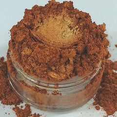 Loose powder makeup with bronze and gold shimmer in a clear glass jar, spilled on white surface