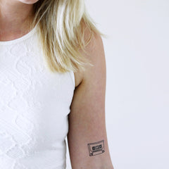 Close-up of hand applying skin-safe cassette tape temporary tattoo with precision on glowing forearm