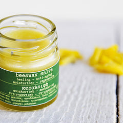 Beeswax salve in a glass jar with yellow contents and a green label on a white wooden surface