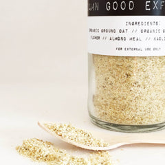 Exfoliant powder in a glass jar with a wooden spoon, beige powder, Damn Good Exfoliant label