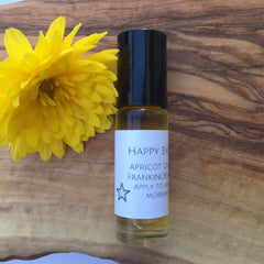 Essential oil bottle with black cap, white label, and yellow flower on wood grain background
