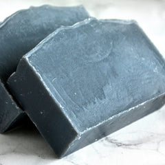 Soap bars, dark gray rectangular bars with rough edges, stacked on white surface