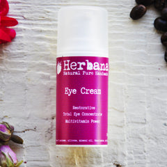 Eye Cream bottle with white cap and pink label, Herbana brand name visible, on white textured surface.