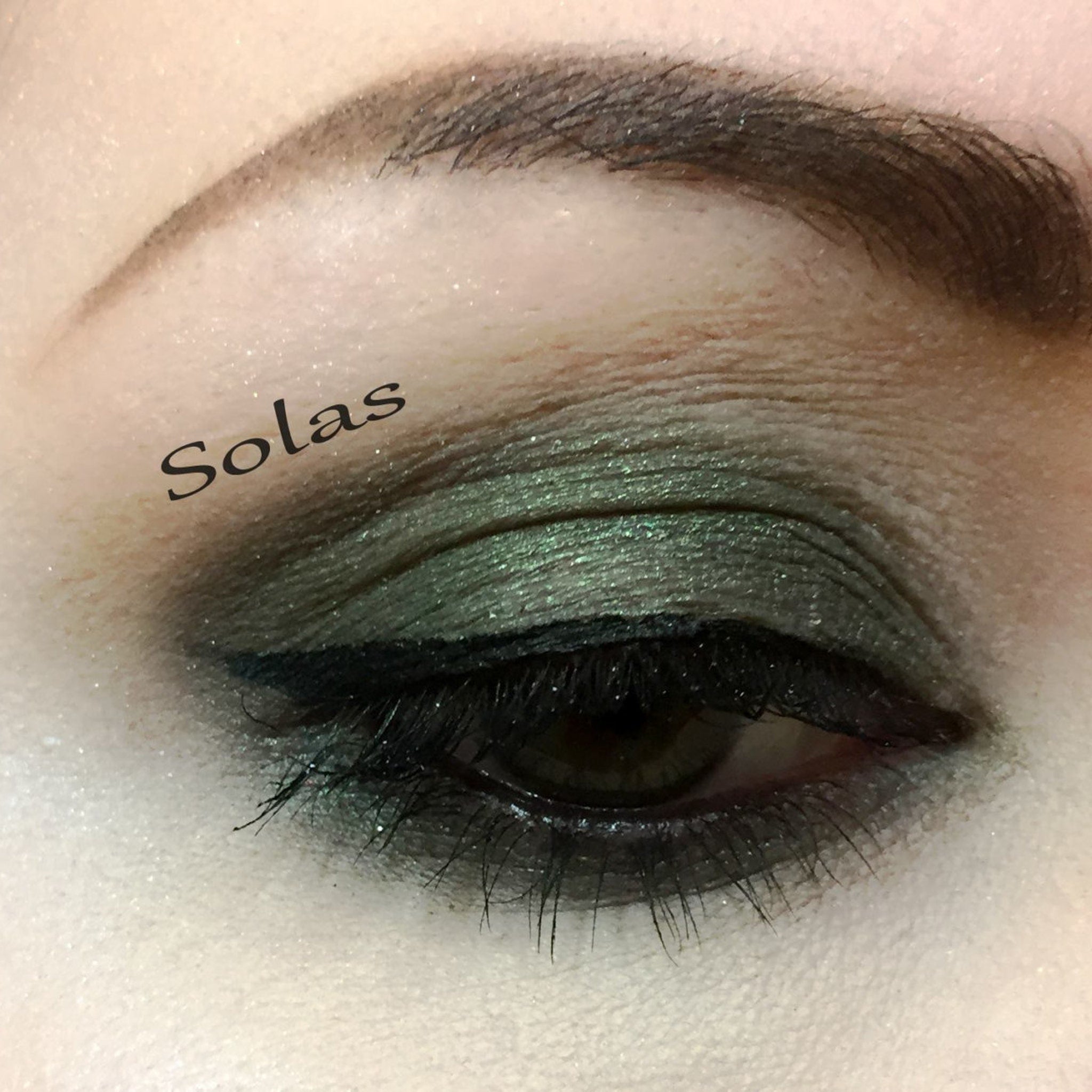 Eye makeup with green eyeshadow, black eyeliner, and Solas brand text on eye