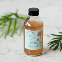 Facial toner bottle with clear glass, brown liquid, and black cap, Ballerina Botanicals label