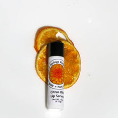 Lip balm with white tube, black cap, and orange dried fruit slices on white surface