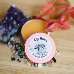 Eye balm in pink tin with "Ninas Bees" label, surrounded by crystals and leaves
