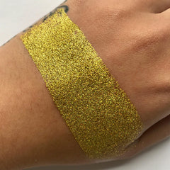 Gold glitter swatch on skin, showing yellow sparkle texture and skin tone contrast