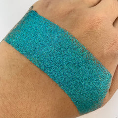 Close-up of vibrant turquoise loose glitter with high-shine metallic particles in a clear jar