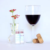 Lip balm tubes with white labels, clear caps, and red tint next to wine glass