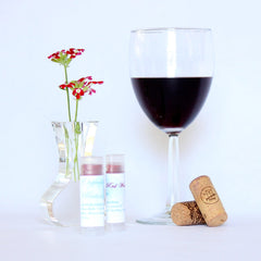 Lip balm tubes with white labels, clear caps, and red tint next to wine glass