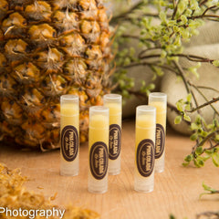 Lip balm tubes with yellow balm, clear plastic, and "Pina Colada" label on wood surface