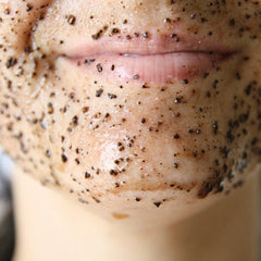 Facial scrub on skin with brown and black particles, close up of lips and face