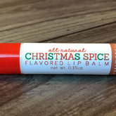 Lip balm tube with red and white label, "CHRISTMAS SPICE" text, on wood surface