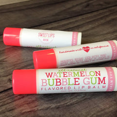 Lip balm tubes with pink caps and white labels, on a wooden surface, with text visible