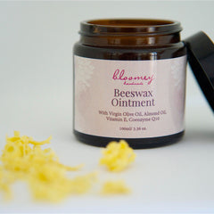 Beeswax ointment in brown glass jar with black lid, "bloomey handmade" label, and yellow wax pieces