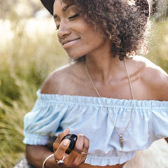 Woman wearing blue off-the-shoulder top with gold necklace and holding black object near water spray