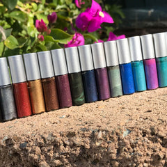 Eyeliner tubes in various glitter colors with silver caps, arranged on a stone surface