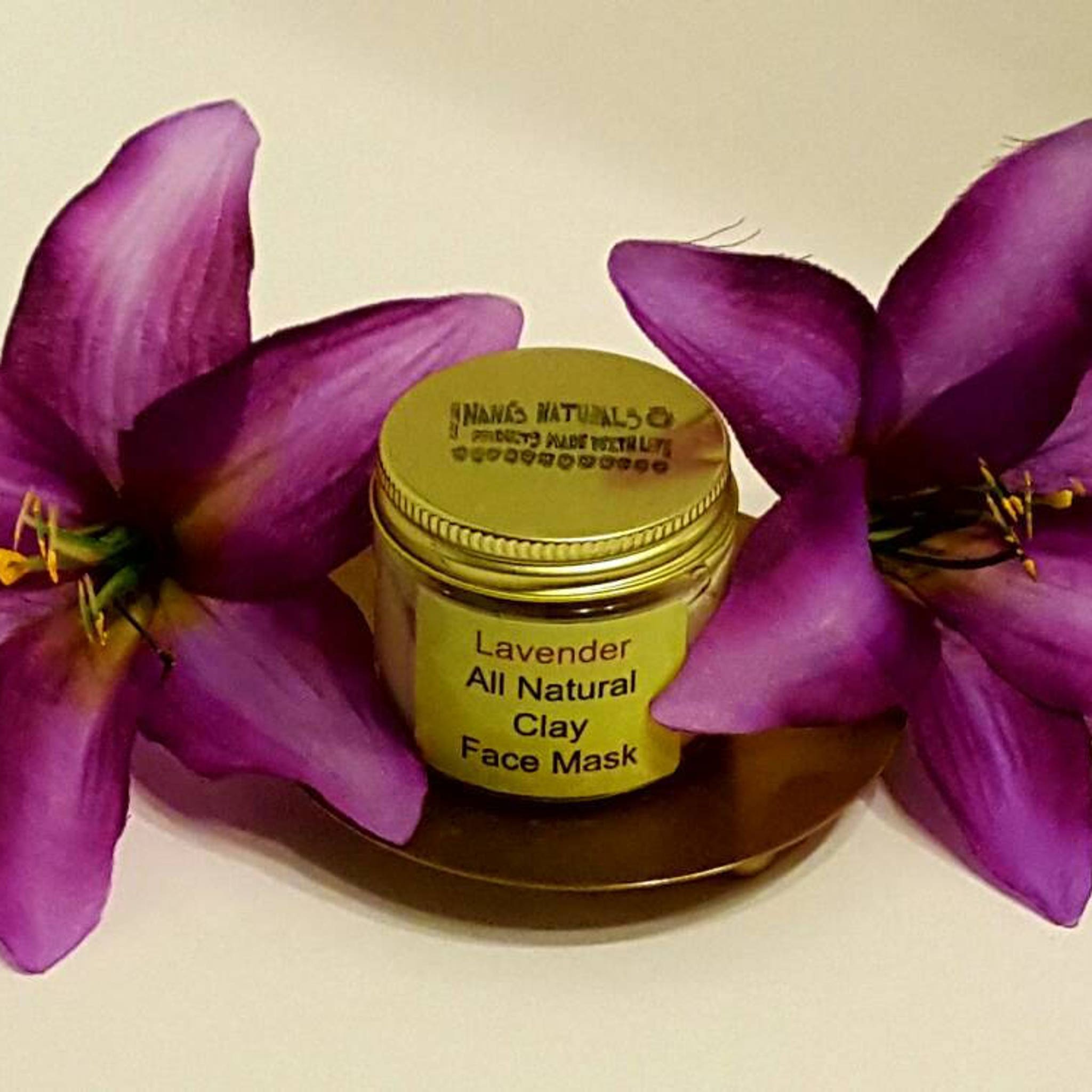 Clay face mask jar with gold lid and purple flowers, Nana's Naturals branding visible