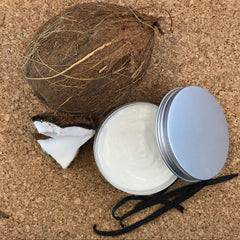 Hand scooping rich vanilla coconut body butter from a white jar onto bare skin