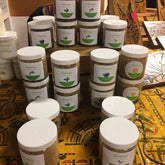 Facial scrub jars, clear plastic with white lids, FloEssence labels, on a yellow patterned surface