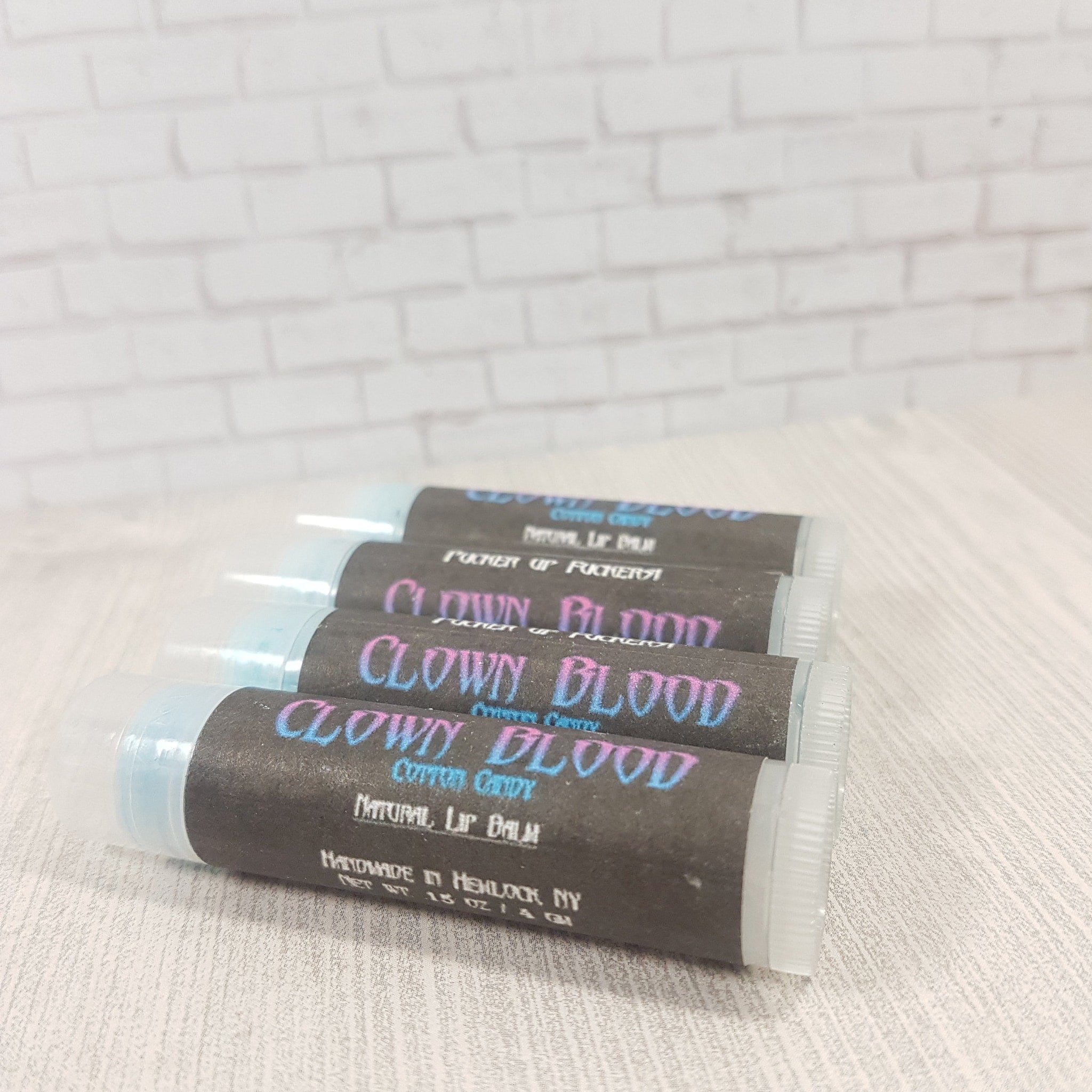 Lip balm tubes with black labels, blue and pink text, and clear caps, stacked on a white surface
