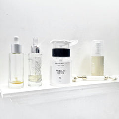 Skincare products in clear, glass bottles with white and silver caps, on a white shelf