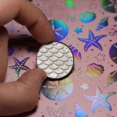 Eye shadow, silver shimmer with scale pattern, held in hand