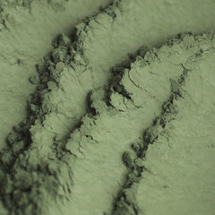 Close-up of matte khaki green eyeshadow being applied to eyelid with a fluffy brush