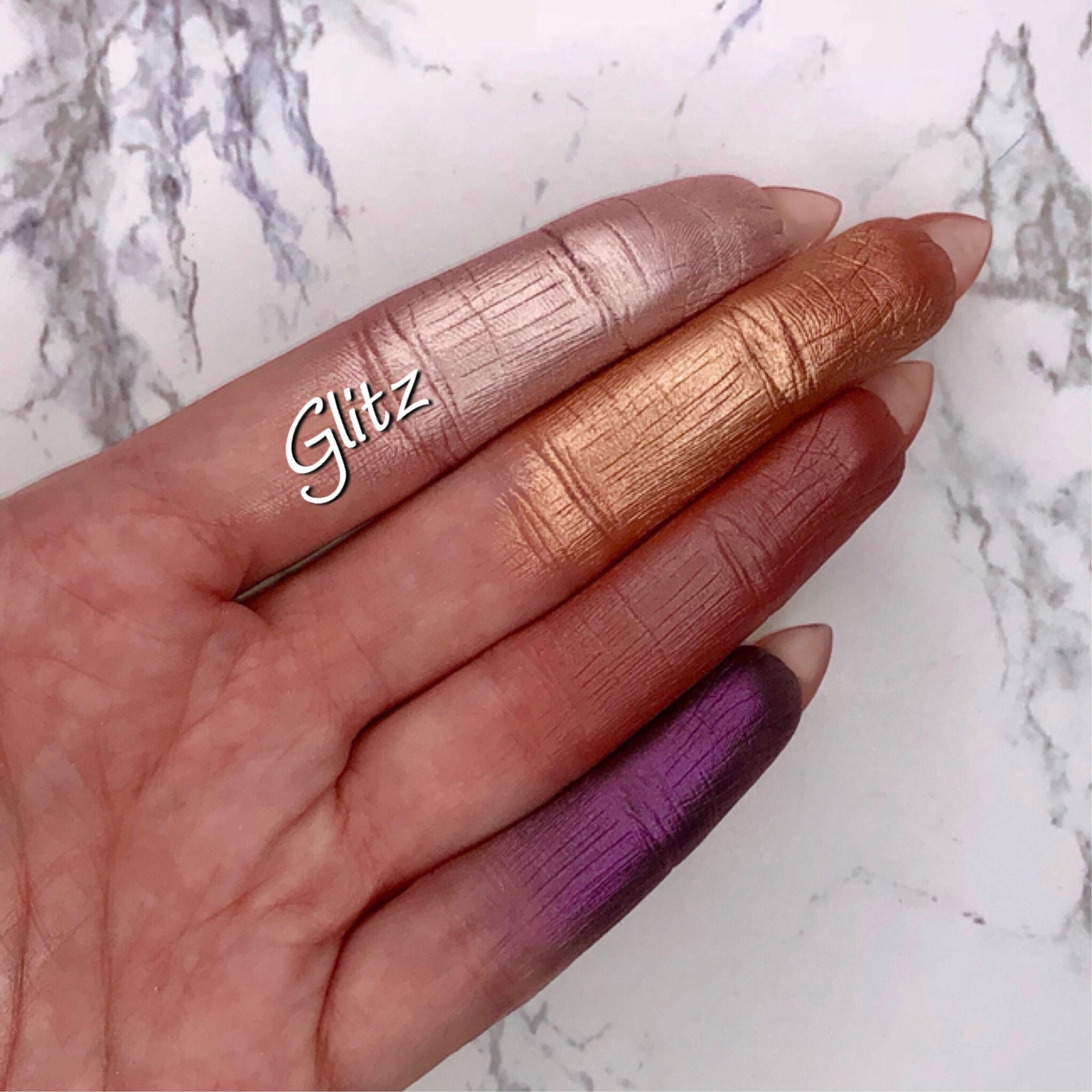 Eyeshadow swatches with metallic finish in pink, gold, red, and purple on fingers, Glitz brand