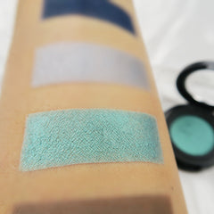 Hand applying shimmering mermaid green eyeshadow with fingertip for bold eye makeup look