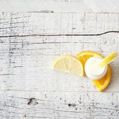 Cream jar with white and yellow fruit slices on a distressed, white wood surface