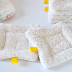 Stack of three organic cotton sponge wipes in soft beige, folded neatly on a marble surface for gentle skincare cleansing