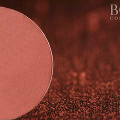 Close-up of fingertips applying deep red wine matte eyeshadow to eyelid with smooth blending motion