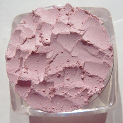 Side view of pastel pink loose powder eyeshadow in a transparent jar with black screw-top lid, showcasing fine shimmer particles.