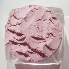 Hand applying pastel pink loose powder eyeshadow with a fluffy brush onto eyelid for soft shimmer effect