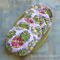 Reusable cotton facial rounds with pineapple print, white stitching, and visible Rocky Mountain Herbs logo