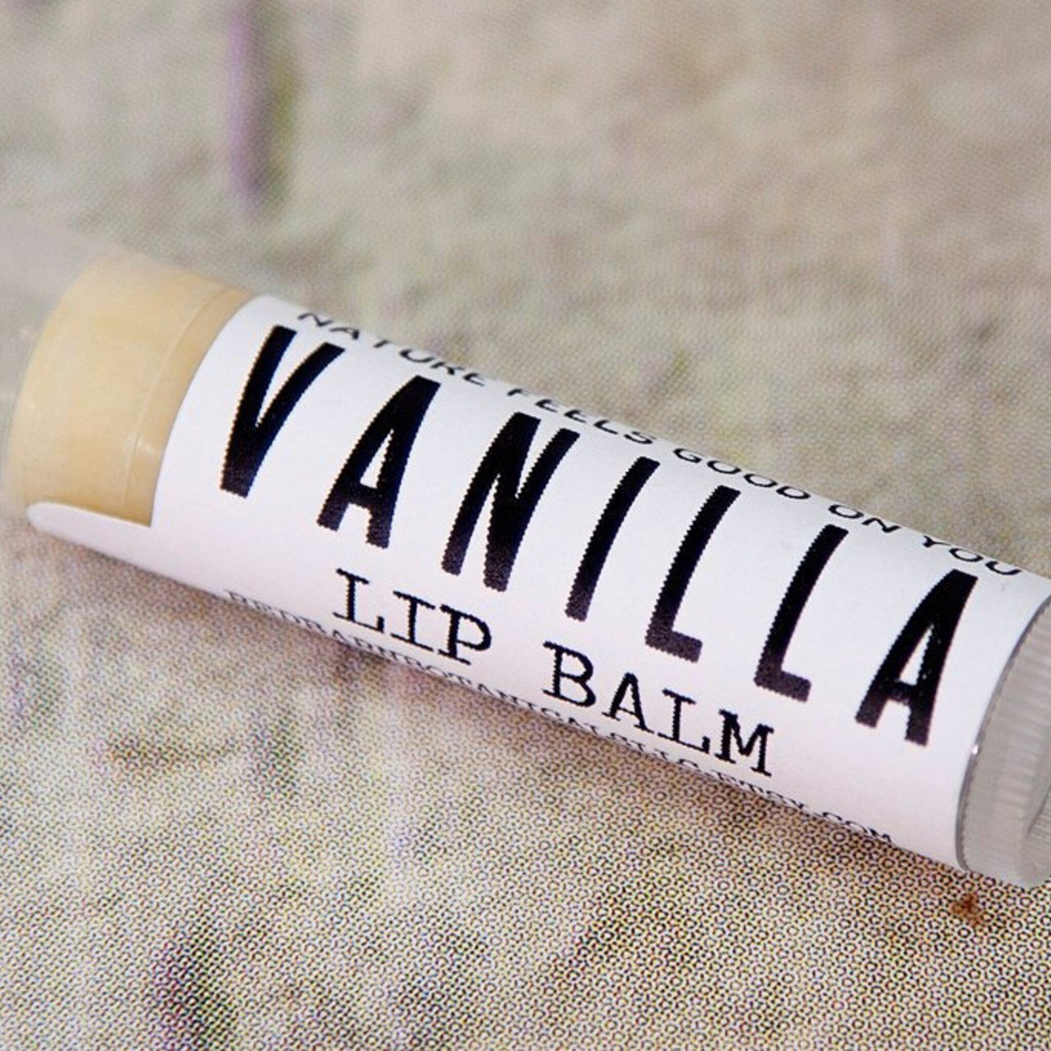 Lip balm tube with white label, black text, and vanilla balm visible