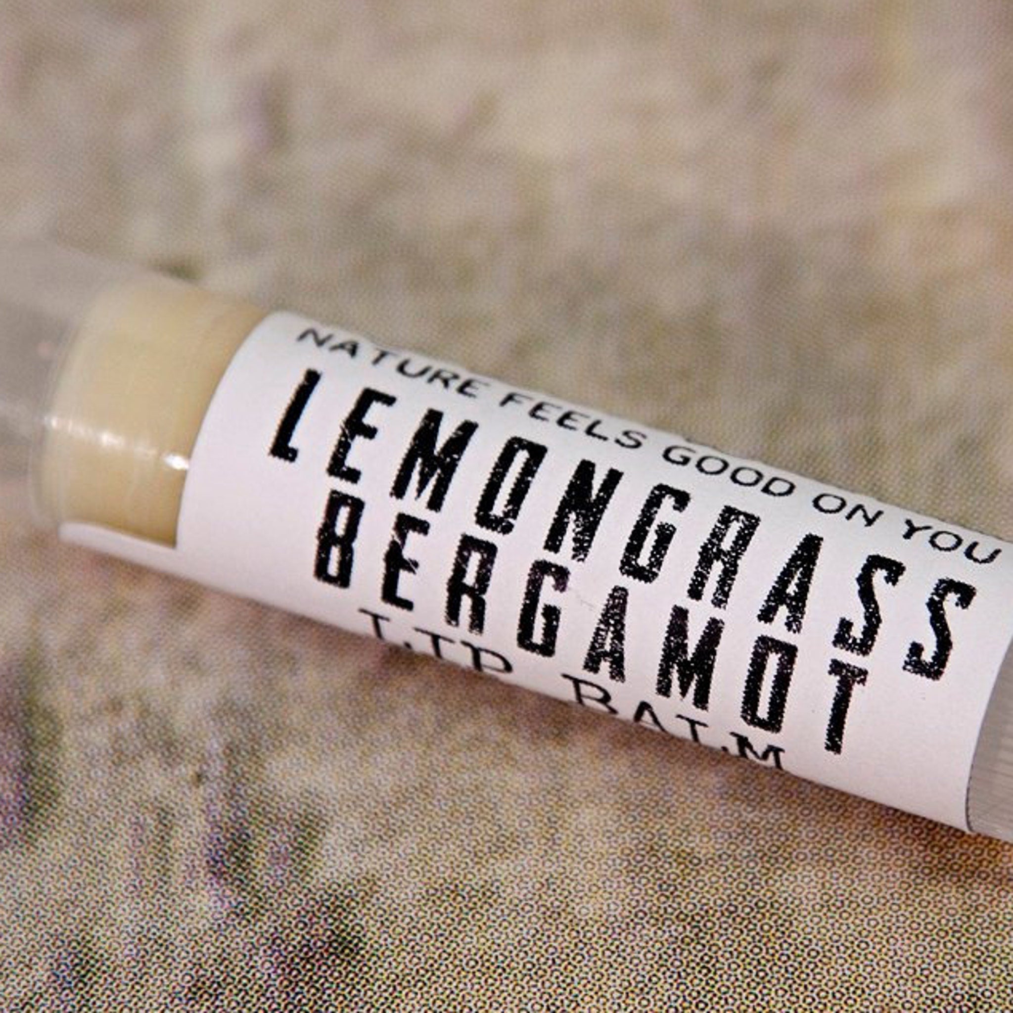 Lip balm tube with white label, black text, and light yellow balm visible