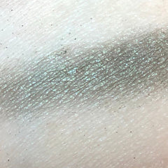 Eyeshadow swatch, shimmery silver-green color, textured surface, on skin