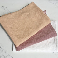 Cloth napkins in beige, mauve, and white linen fabric, folded and stacked