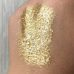Gold glitter swatch on skin, showing texture and color, with light reflecting off the particles