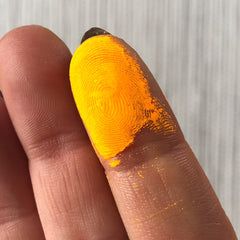 Hand applying vibrant neon orange eye shadow pigment with fingertip for bold makeup look
