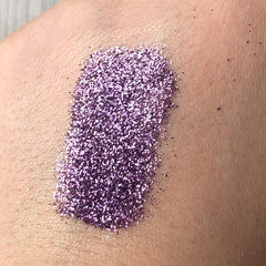 Purple glitter swatch on skin, showing fine particles and texture detail
