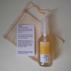 Face tonic bottle with yellow and clear label, with a beige pouch and string above it.