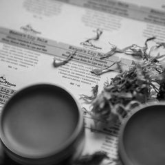 Lip balm tin with blurred gray metal container, paper background, and dried leaves