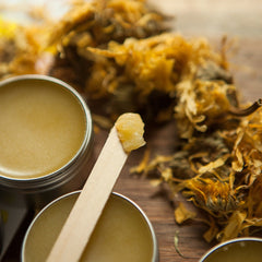 Balm in metal tins, yellow color, wooden applicator, with dried flowers nearby